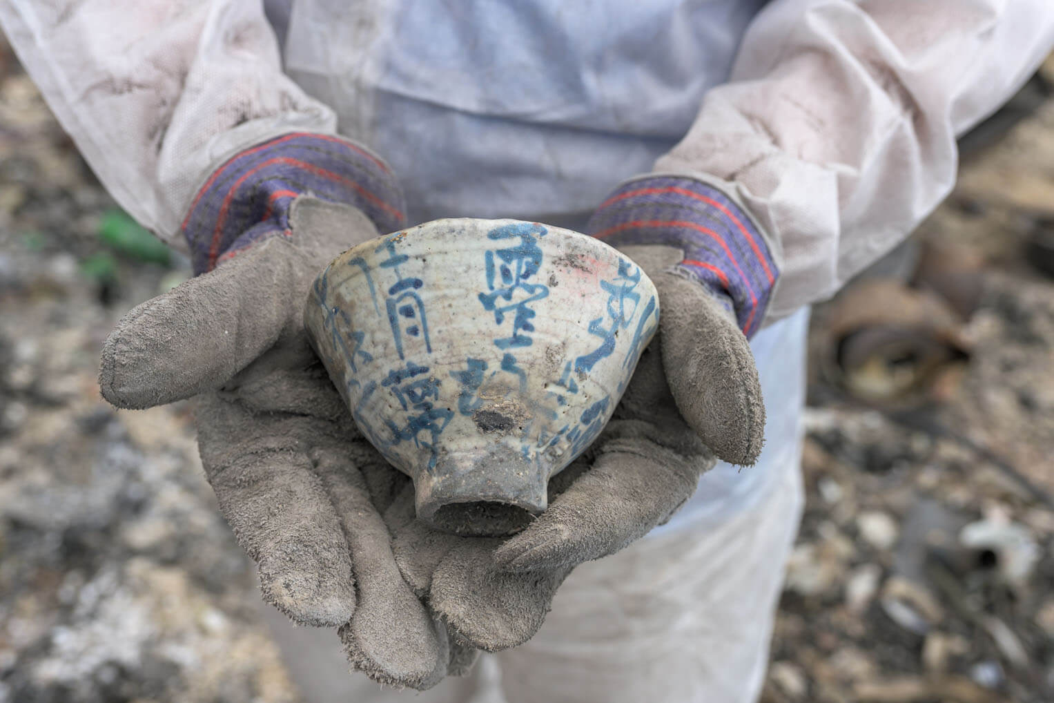A soot-covered Samaritan's Purse volunteer holds an ornate ceramic cup discovered amid the ashes of a home.